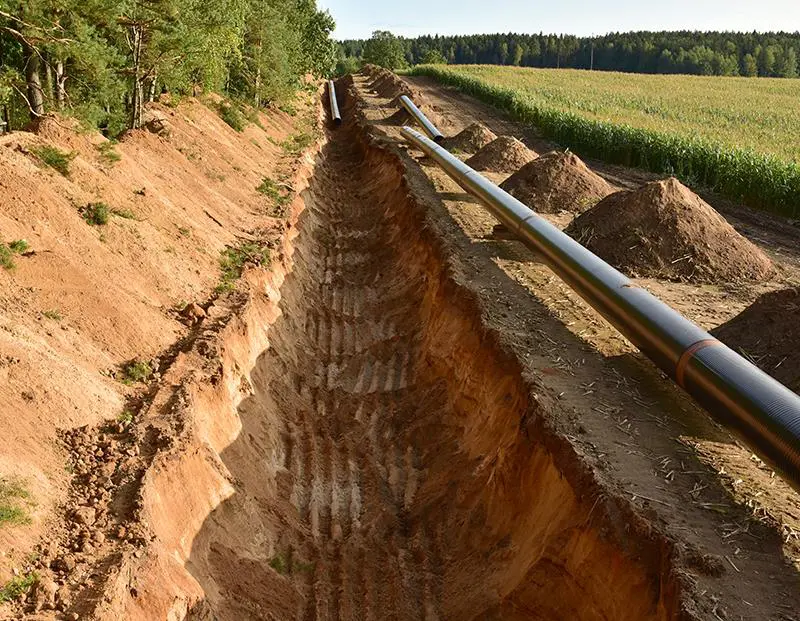 A man is standing in the dirt next to a pipe.